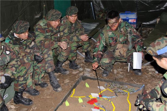 김봉수 중대장(왼쪽 두번째)이 실제지형을 축소한 모형판에 공격작전을 설명하고 있다.