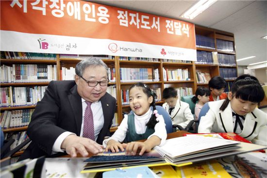한화그룹 김연배 부회장이 수유동 한빛맹학교에서 어린이들에게 점자도서 등 시각장애인용 특수도서를 전달하고, 어린이들과 도서관에서 함께 책을 읽고 있다.
