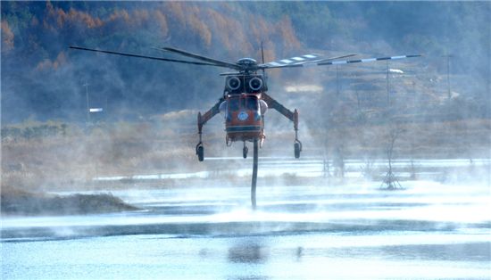 저수지에서 산불 끄기에 쓸 물을 빨아올려 담고 있는 초대형 산림헬기(S64E). 