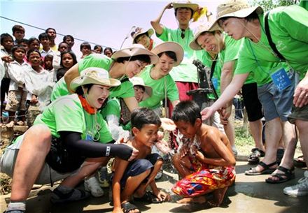웅진코웨이의 캄보디아 우물파기 봉사단이 현지에서 어린이들에게 깨끗한 물을 제공하면서 활짝 웃고 있다.