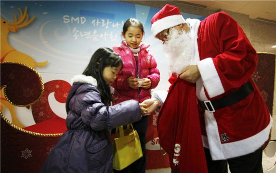 산타 복장을 한 조수인 사장이 22일 저녁 천안시 남서울대학교 실내체육관에서 열린 'SMD 사랑나눔 송년음악회'에서 어린이들에게 선물을 나눠주며 격려하고 있다.