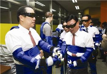 우리투자증권 황성호 사장(맨 왼쪽)이 지난 14일 성남에 위치한 고령친화종합체험관에서 80세 노인의 신체활동 및 시력 수준과 비슷한 노인생활 체험복을 착용한 채 고령자들의 불편함을 체험하고 있다.