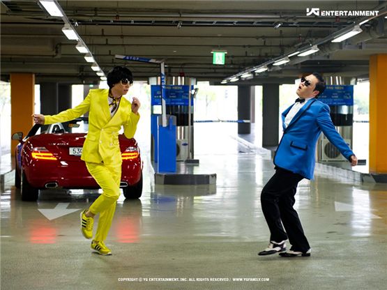 Korean comedian Yoo Jae-suk (left) donned in a bright yellow suit and singer PSY dances together in a scene of his music video to his song "Gangnam Style." [YG Entertainment]