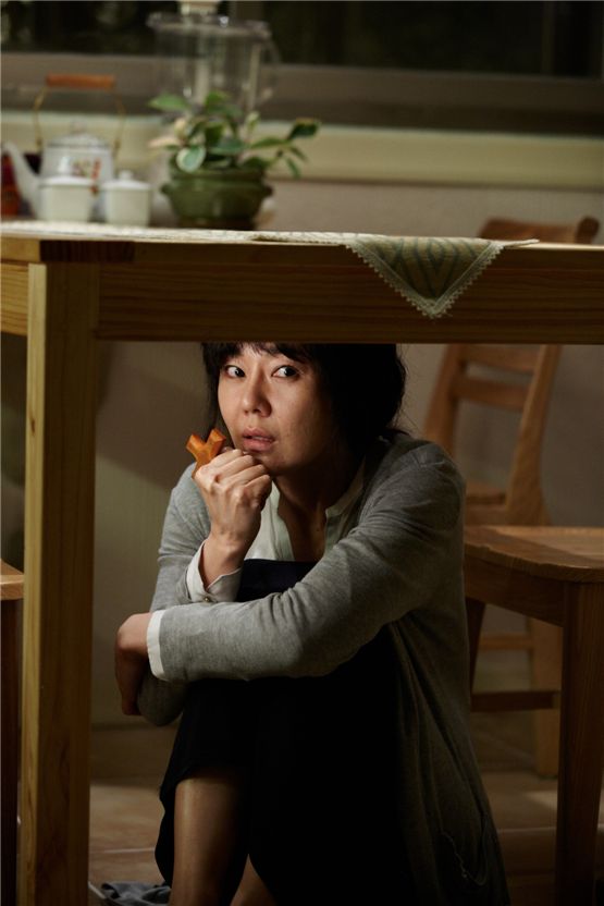 Actress Kim Yun-jin as her character Song Kyung-hee acts scared and hides under a table after the ghost of her dead stepdaughter visits her every day in the movie "My Neighbor" set to hit local theaters on August 23, 2012. [Lotte Entertainment]