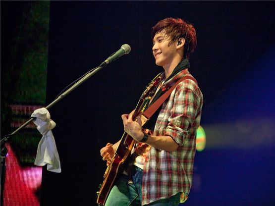 FTIsland's guitarist Song Seung-hyun, donned in a plaid shirt and jeans, smiles as he pays the guitar during their concert "TAKE FTISLAND," which took place at Seoul's Olympic Hall on September 1 and 2, in front of several thousand fans. [FNC Entertainment] 