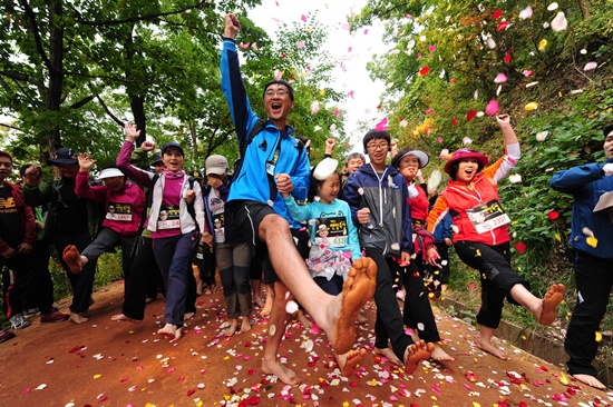 맨발걷기대회에 참가한 가족, 선수단이 꽃잎이 휘날리는 황톳길을 걷고 있다.