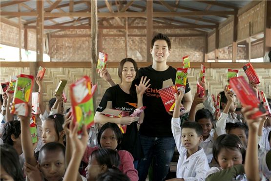Actress Kim Hyo-jin (left) and Yoo Ji-tae (right) pose together amongst children holding up their school supplies received from the pair in the picture released by Namoo Actors on December 5, 2012. [World Vision]