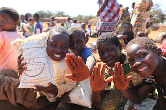 아프리카 말라위 어린이들이 뉴스킨 엔터프라이즈가 제공한 영양식사 '바이타밀'을 들고 환하게 웃으면 손을 흔들고 있다.