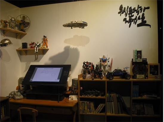 전시실에 설치된 '웹툰작가 작업실' 모습. 디지털 작업 책상과 책장들. 