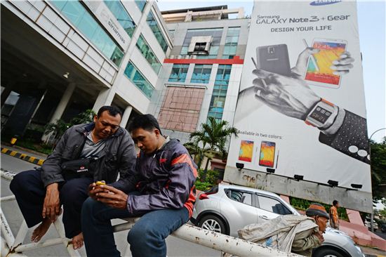삼성전자 갤럭시 스마트폰 광고 앞에서 한 인도네시아 남자가 옆 사람에게 스마트폰을 보여주고 있다. 사진=블룸버그
