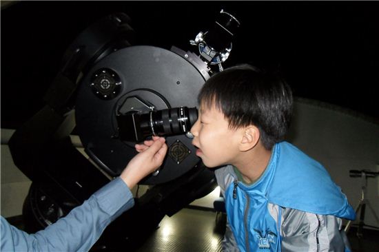 어린이가 천체 망원경으로 하늘의 별자리를 관측하고 있다. 