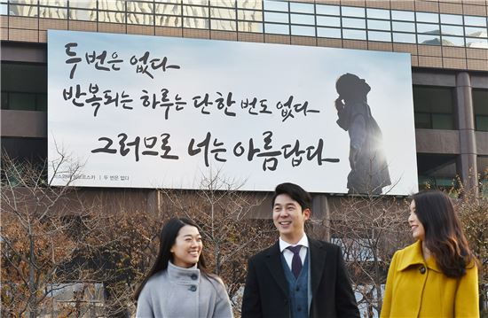 서울 광화문 교보생명빌딩에 걸려 있는 광화문글판 겨울편 앞으로 사람들이 지나가면서 활짝 웃고 있다.  