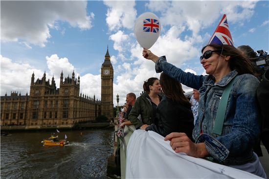 ▲15일(현지시간) 영국 런던 템즈강의 웨스트민스터 다리에서 영국 국기가 그려진 모자를 쓴 한 여성이 풍선을 흔들며 시위대를 응원하고 있다. 이날 템즈강에서는 EU가 영국 어업을 망치고 있다고 주장하는 브렉시트 찬성파와 이에 동의하지 않는 반대파가 맞서 해전 시위를 벌였다.(사진=블룸버그)
