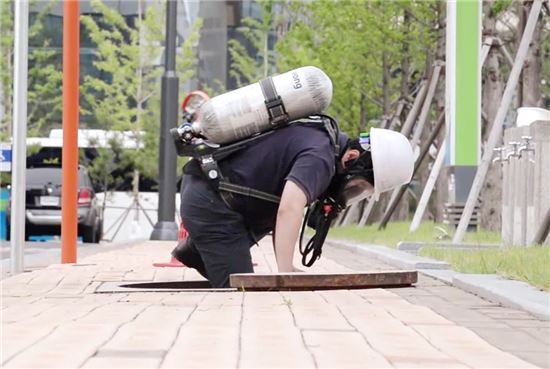 근로자가 질식재해 예방 보호장비를 착용한 후 밀폐공간인 맨홀에서 작업하기 위해 들어가고 있다. 
