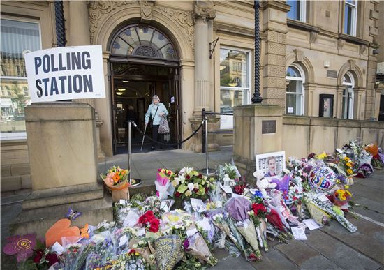 한 여성이 브렉시트 반대 운동을 하던 중 피습을 당해 사망한 조 콕스 의원을 추모하는 꽃다발들이 놓여진 영국 요크셔의 투표소를 나서고 있다. 요크셔는 조 콕스의원의 출신지이다. (AP=연합뉴스)