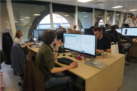사타고의 직원들이 컴퓨터 모니터 너머로 대화를 나누며 일하고 있다.