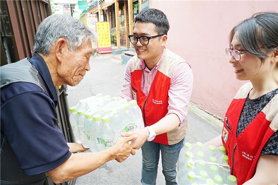 20일 오후 세븐일레븐 봉사단원들이 서울역 쪽방촌에 거주하는 어르신에게 생수를 나눠주고 있다.