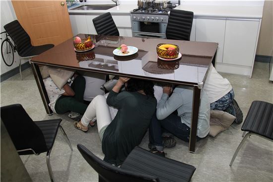 동작구 보라매안전체험관 지진체험에 참여한 시민들이 지진 상황을 가정해 식탁 아래로 피신하고 있다.