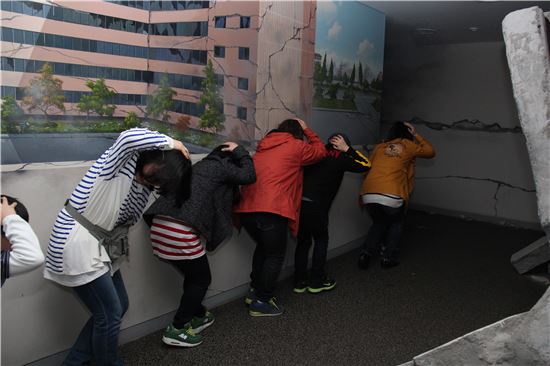 지진체험에 참석한 시민들이 흔들리는 복도를 지나가며 손으로 머리를 보호하고 있다.