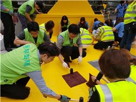동부화재 직원들이 서울시내 학교 인근에서 횡단보도 신호대기공간을 노란색으로 구획하는 옐로카펫을 설치하고 있다.