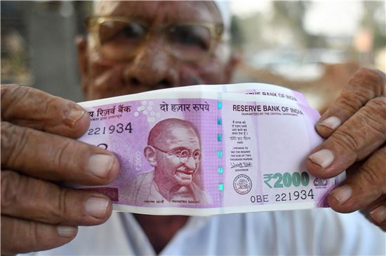 인도 우타르프라데시주(州) 다드리의 어느 은행에서 한 주민이 구권과 교환한 2000루피짜리 신권 지폐를 들어 보여주고 있다(사진=블룸버그뉴스).