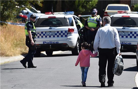 ▲23일 호주 멜버른에서 경찰이 테러모의자들의 집을 급습한 가운데 경찰차들이 서있는 도로로 남성과 어린이가 걸어가고 있다. 