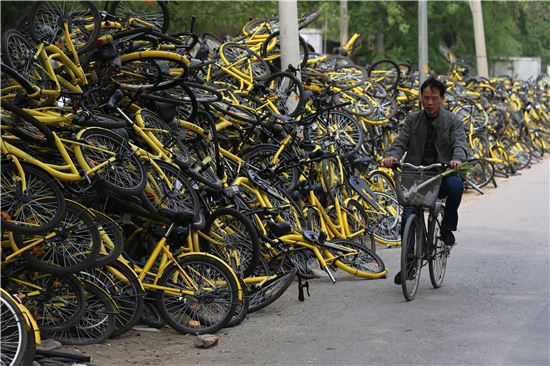 중국 베이징에 거주하는 한 중국인이 공유 자전거 회사 오포의 수리 센터에 수북이 쌓인 고장 난 자전거 옆을 지나고 있다.[사진=EPA연합]