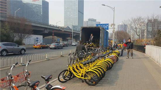 중국 최대 공유 자전거 회사 오포가 베이징 도심에 새 노란색 자전거를 실어 나르고 있다. 이 자리에 있던 경쟁사 모바이크의 주황색 자전거와 어우러진 모습.