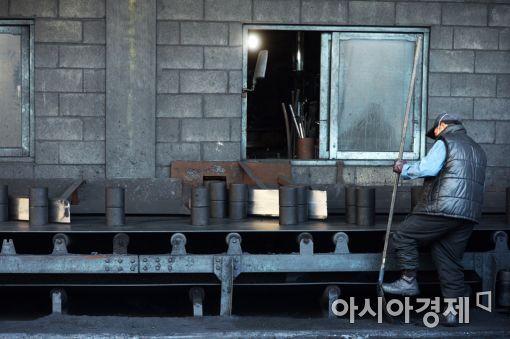 연탄공장에서 한 직원이 바닥에 떨어진 불량 연탄을 청소하고 있다. 