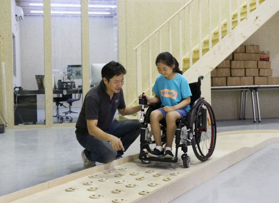 심재신 토도웍스 대표가 토도웍스 사옥에 위치한 휠체어 전용 교육장에서 장애 아동에게 수동휠체어용 전동 키트를 활용한 이동 교육을 진행하고 있다.  [사진= SK행복나눔재단 제공]