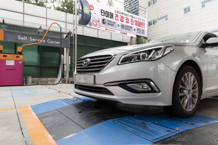 SK네트웍스의 종합 차량관리 브랜드 스피드메이트가 '타이어 건강검진' 캠페인을 진행한다. 사진은 한 자동차가 바닥에 장착된 타이어 마모도 측정장비(파란색)를 통과하며 타이어 검진받는 모습.