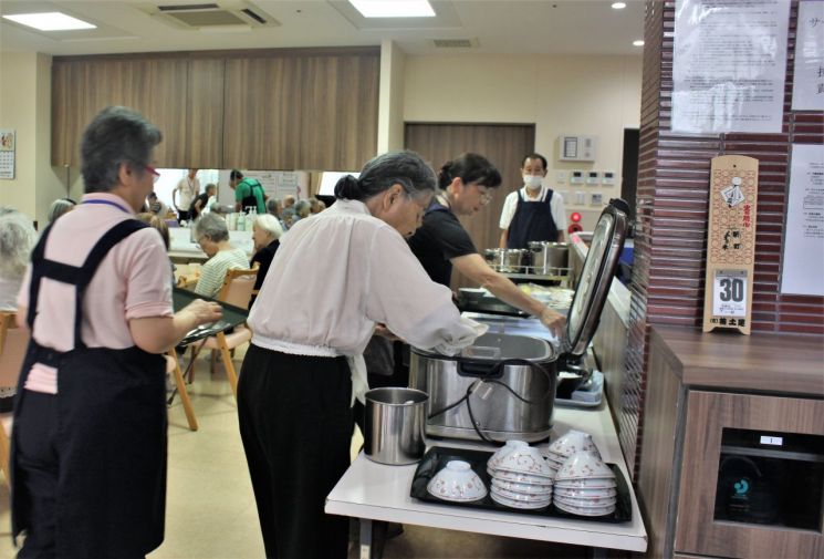 데이케어 서비스를 이용하는 노인들이 식판에 밥과 반찬을 담고 있다.