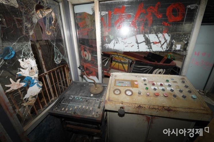 세월의 흔적이 느껴지는 디스코팡팡 놀이기구 관리실. 창문이 날카롭게 깨져 있다. 녹슨 제어기 너머 놀이기구가 한산한 모습이다. /문호남 기자 munonam@