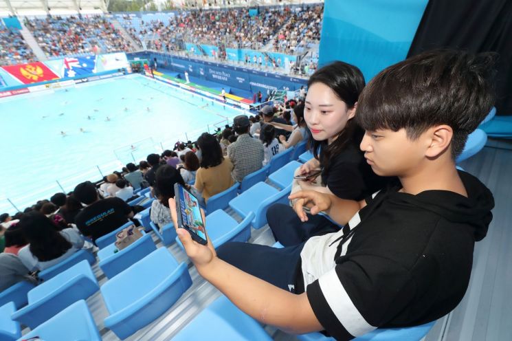KT는 ‘2019광주FINA세계수영선수권대회’에 준비한 5G 네트워크와 5G ICT 체험관을 통해 전세계 관람객들에게 5G 기술을 선보였다고 22일 밝혔다. 광주세계수영선수권대회 참석한 관람객들이 KT 5G 네트워크를 이용해 스마트폰으로 경기 동영상을 감상하고 있다.