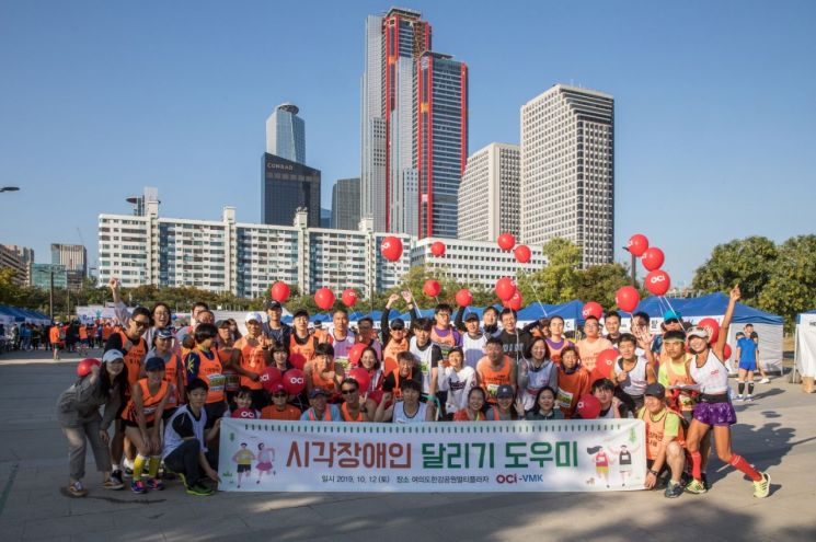 ▲지난 12일 여의도한강공원에서 열린 시각장애인 마라톤대회에서 참가자들과 OCI 봉사자들이 단체사진을 찍고 있다.
