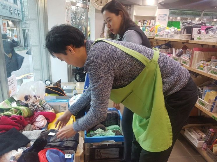 서울 강남구 도곡동에 위치한 아름다운가게 양재점에서 발달장애인 오성민(27·가명)씨가 기부 물품으로 들어온 목도리를 정리하고 있다. 권수정 잡코치가 잘하고 있다며 격려하는 모습. (사진=이현주 기자)
　