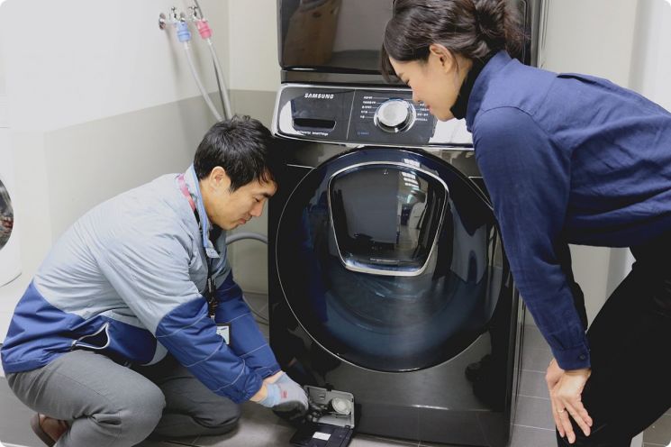삼성전자서비스 수리 엔지니어가 출장 점검 서비스를 신청한 고객에게 '플러스 원 케어 서비스'의 일환으로 드럼세탁기 배수펌프 잔수 제거 방법을 설명하고 있다.