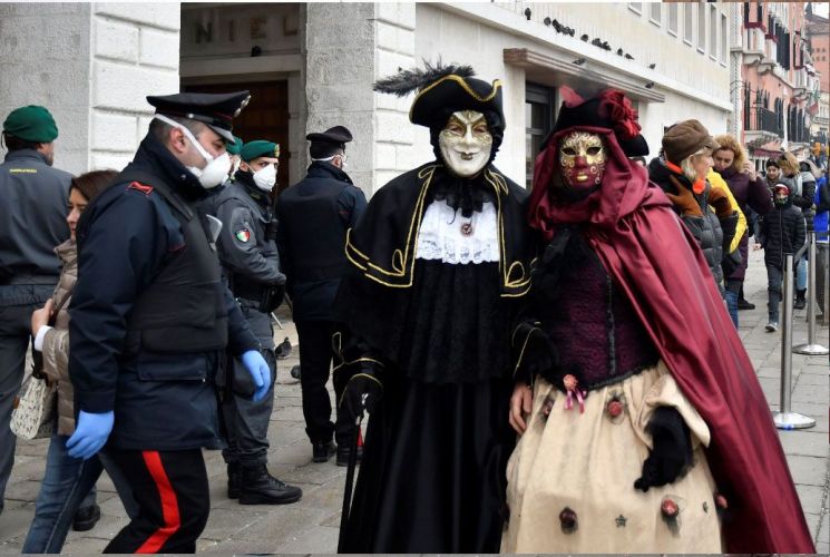 23일(현지 시각) 마스크를 쓴 이탈리아 경찰관이 베니스 축제에 참가한 사람들 옆을 지나고 있다. /AP=연합뉴스