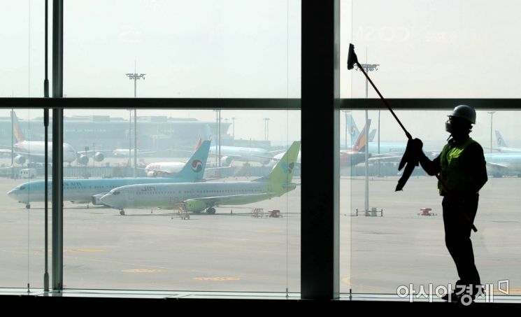 9일 인천국제공항 2터미널에서 한 관계자가 창문을 닦고 있다. 창문 너머로 운행을 중단한 항공기들이 계류돼 있다. /문호남 기자 munonam@