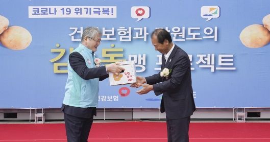 김용익 국민건강보험공단 이사장(왼쪽)이 22일 건보공단 원주사옥에서 열린 '감자동맹(감동) 프로젝트' 행사에서 최문순 강원도지사로부터 감자 상자를 건네받고 있다./사진 제공=건보공단