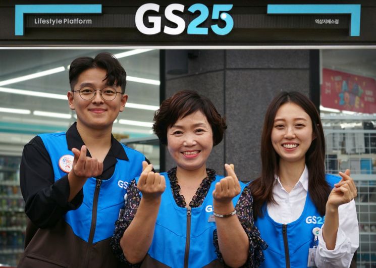 GS25 직원들과 경영주가 미소지으며 하트를 그려보이고 있다.