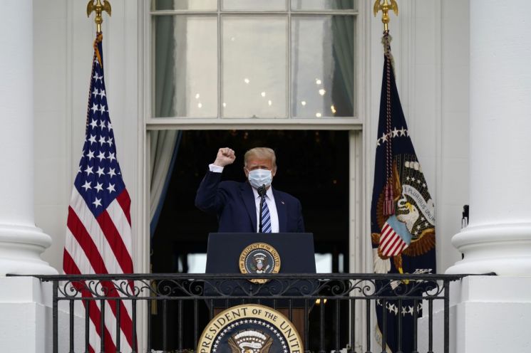 도널드 트럼프 미국 대통령이 10일(현지시간) 마스크를 쓴 채 백악관 블루룸 발코니에 도착, 지지자들을 향해 주먹을 불끈 쥐어 보이고 있다. / 워싱턴 AP=연합뉴스