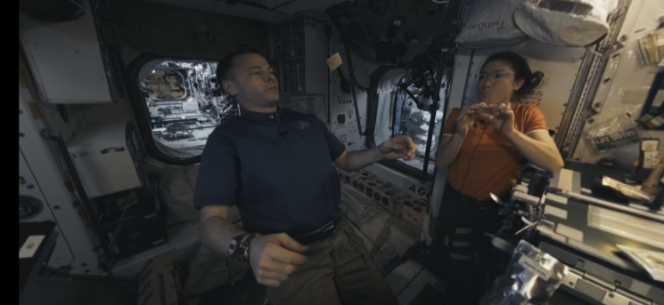 한 우주비행사가 자신 쪽으로 천천히 다가오는 크래커를 받아먹고 있다. 우주 공간에서만 가능한 '무중력 식사' 장면이다.