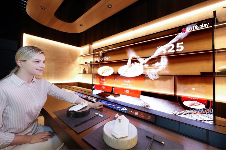 LG디스플레이가 CES 2021에서 선보이는 '레스토랑 존'에서 모델이 투명 OLED를 이용해 메뉴를 살펴보고 있다.