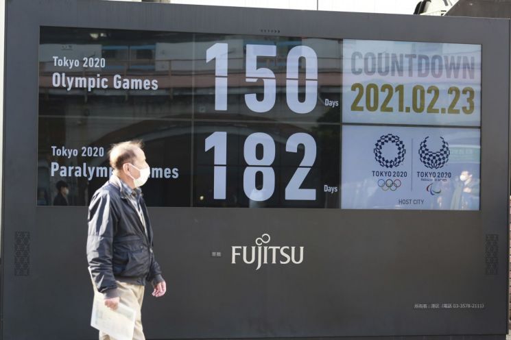 23일 일본 도쿄 시내에서 마스크를 쓴 한 행인이 올림픽 개최가 150일 앞으로 다가왔음을 알리는 전광판 주변을 지나가고 있다. [이미지출처=AP연합뉴스]