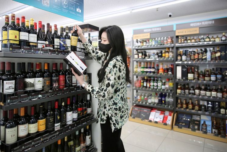 GS25의 와인25플러스 플래그십스토어 1호점 역삼홍인점 매장에서 고객이 카탈로그와 와인을 살펴보고 있다.