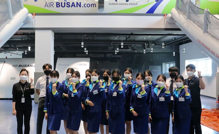Professional instructors and students are taking a commemorative photo at the Air Busan training facility.