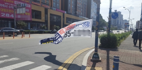 전남 무안군 삼향읍 남악마루삼거리에 걸어놓은 아파트 분양 홍보 현수막 한쪽이 떨어져 바람에 나부끼면서 운전자와 보행자들에게 불편을 주고 있다. / ⓒ 아시아경제