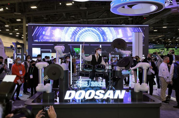 두산로보틱스가 CES 2022에서 로봇 드럼 공연을 선보인 가운데 드러머가 협동로봇에 연결된 전자 심벌과 함께 연주하고 있다.[사진제공=두산]