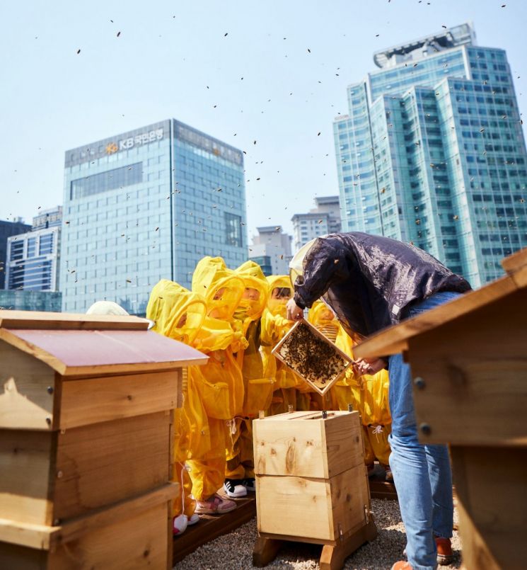 KB금융그룹 직원 가족들이 KB국민은행 본관 옥상에 설치된 ‘K-Bee’ 도시 양봉장에서 벌 키우기 체험 활동을 하고 있다. 사진=KB금융 제공